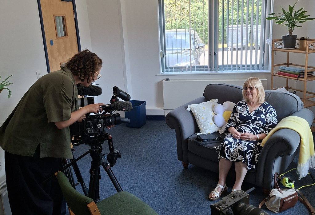 Sheila sat on a sofa being filmed by a camera